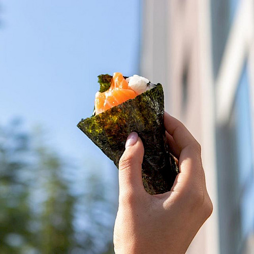 Person holding salmon sushi hand-roll